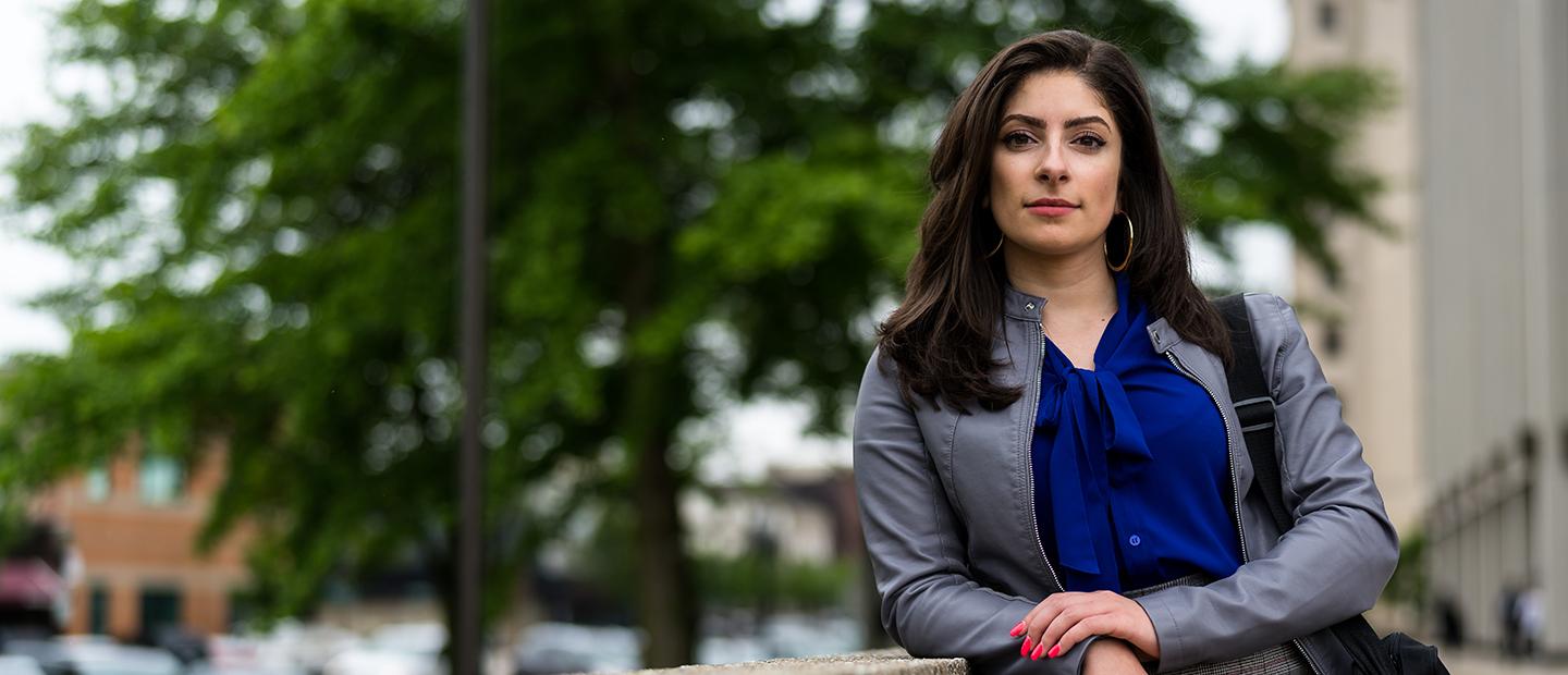 A woman standing outside, leaning on a railing, looking directly at the camera.